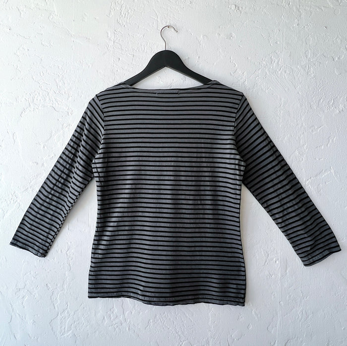 Black and gray striped long-sleeve shirt on a hanger against a white wall as viewed from the back