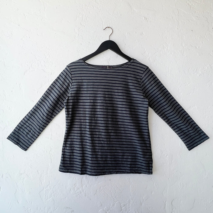 Black and gray striped long-sleeve shirt on a hanger against a white wall