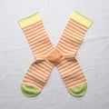 Adobe Striped Peach socks by Bonne Maison — fine horizontal peach and cream stripe cotton crew with yellow cuff and lime green heel and toe, flat lay pair crossed on a white linen background