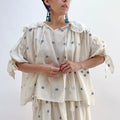 A woman wearing a white top with blue floral print with elbow length sleeves and a large collar with ruffle trim.