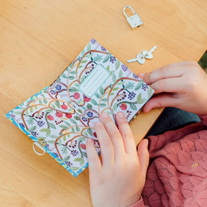 Person opening a floral-patterned journal on a wooden surface with keys and a lock.