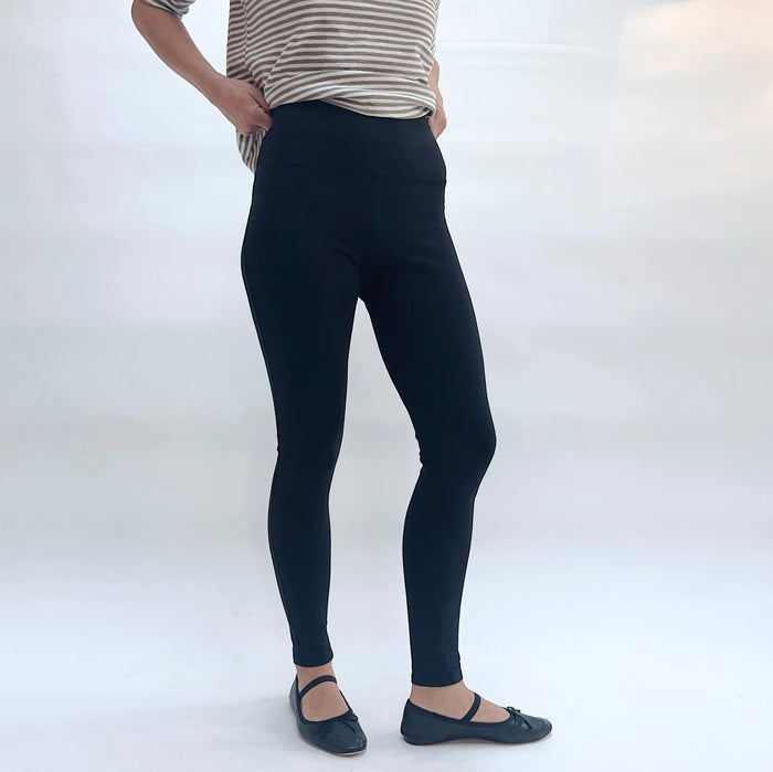 Person wearing black leggings and a striped shirt on a white background