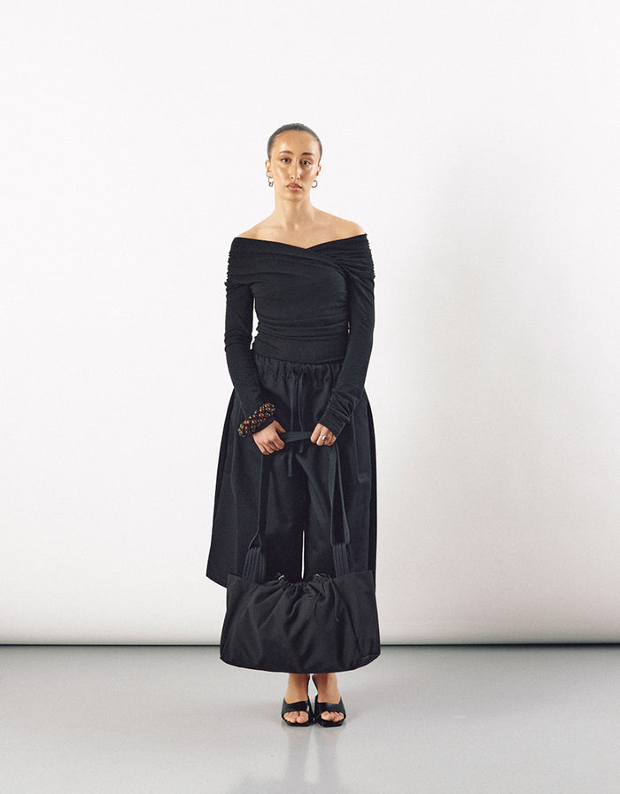 Woman dressed in minimalist black outfit holding a large black tote bag with a soft, voluminous shape, highlighting understated elegance and contemporary design.
