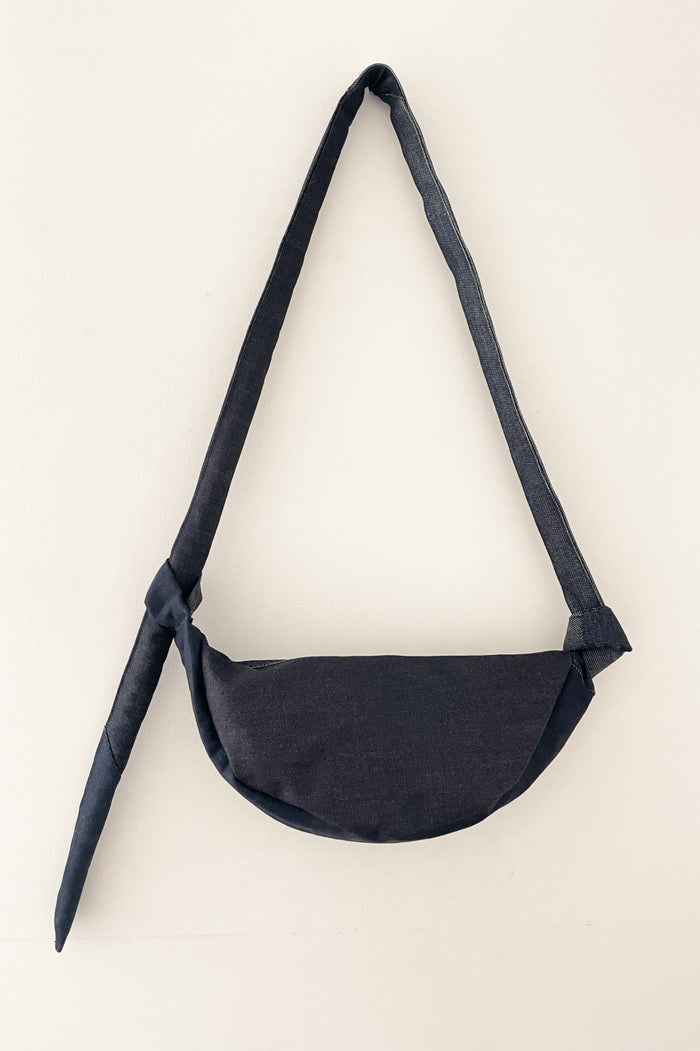 Minimalist unisex denim crossbody bag with asymmetrical volume and a tied strap, crafted with understated elegance and high-quality French design.