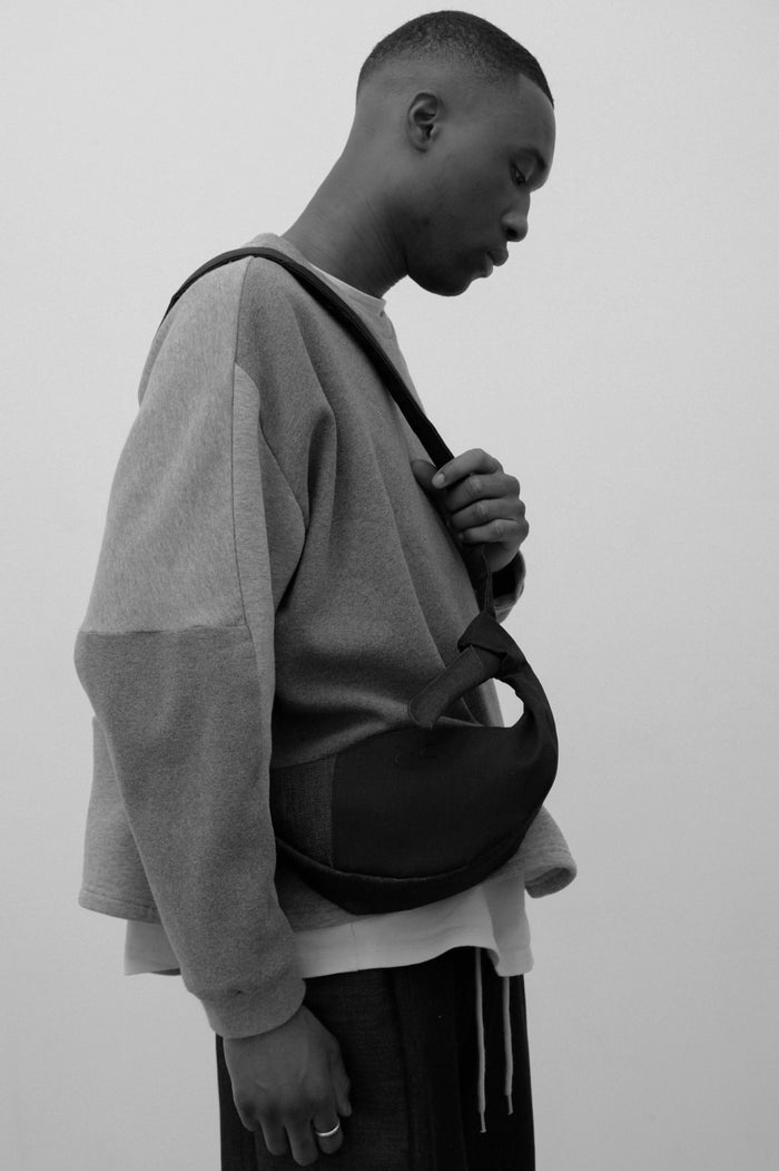 Black and white portrait of a model wearing a minimalist denim crossbody bag with a curved silhouette, paired with a loose, layered outfit emphasizing understated elegance and modern design.