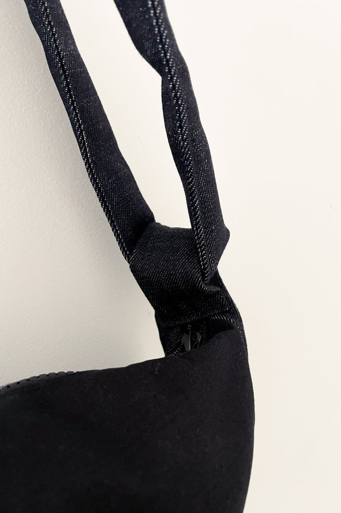 Close-up of a minimalist denim strap attached to a structured black fabric bag, showcasing high-quality craftsmanship and subtle design details.