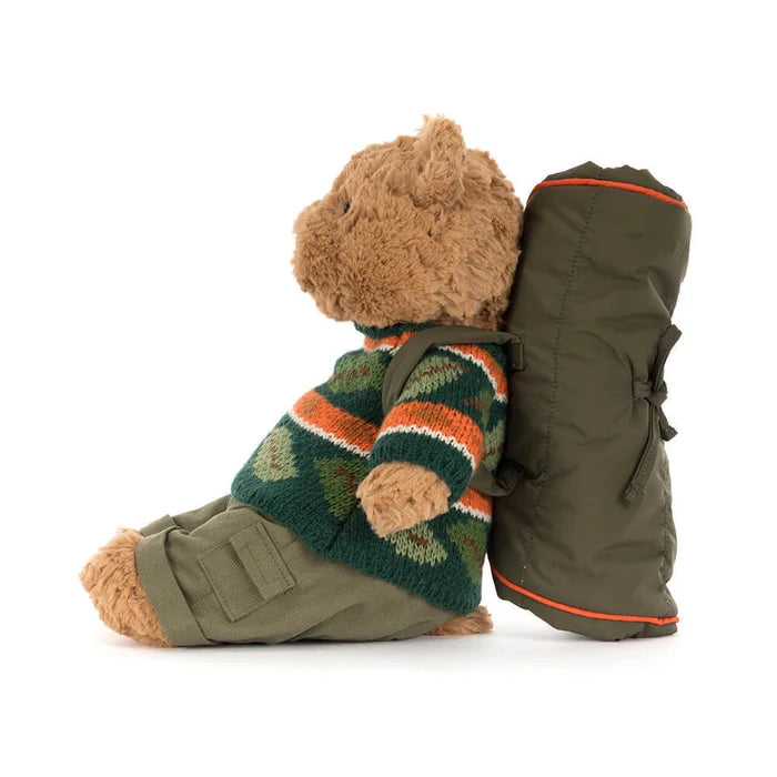 Teddy bear wearing a sweater and carrying a backpack on a white background, viewed from the side