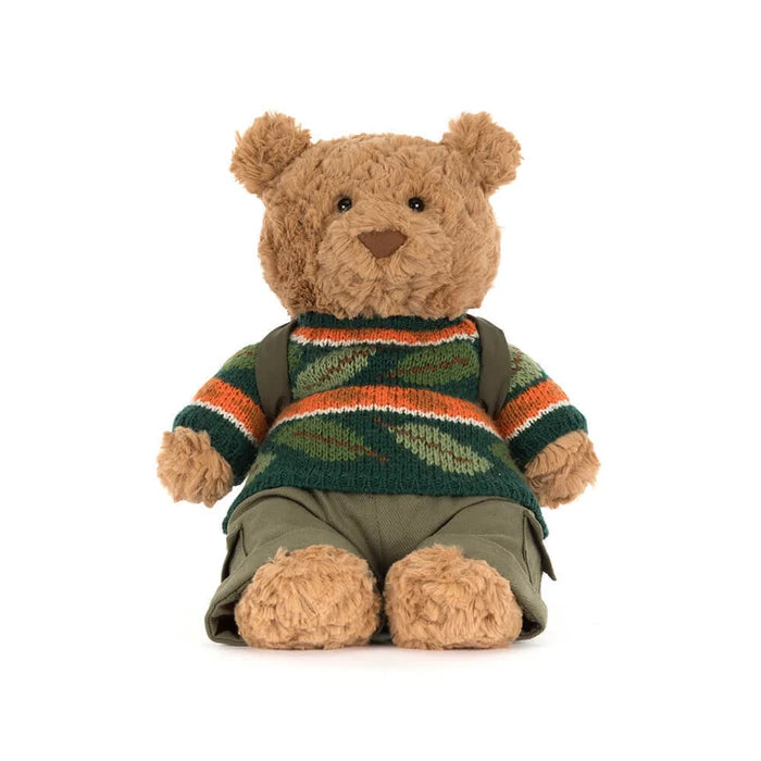 Stuffed teddy bear wearing a patterned sweater and green pants on a white background