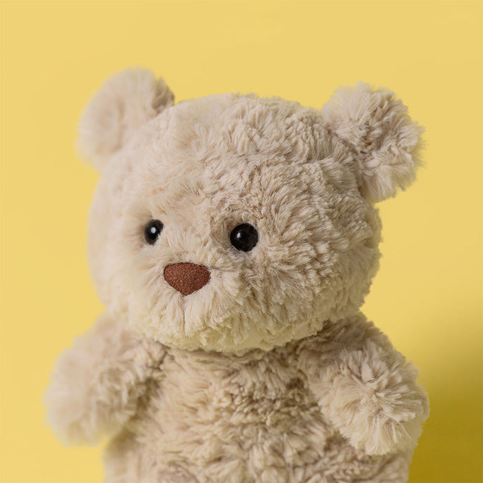 Close-up of Jellycat Bartholomew Bear Junior's face showing soft curly cream fur, black bead eyes, and a brown suede-style nose, against a yellow background