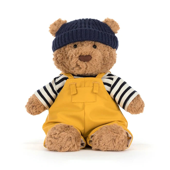 Front-facing view of Jellycat Bartholomew Bear in the full seafarer outfit — navy beanie, striped top, and mustard yellow dungarees — seated with legs out, showing black bead eyes and brown nose, on a white background