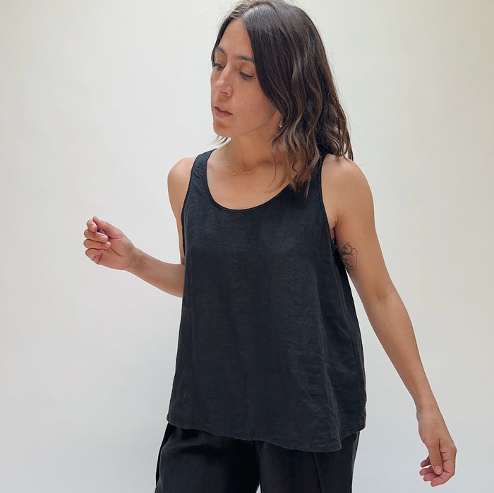 A person with long brown hair wearing a black linen tank top and matching black linen pants.