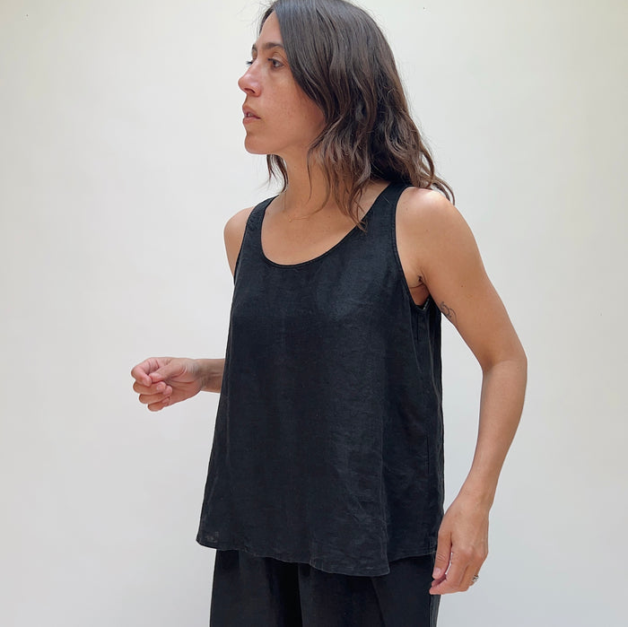 A person with long brown hair wearing a black linen tank top and matching black linen pants.