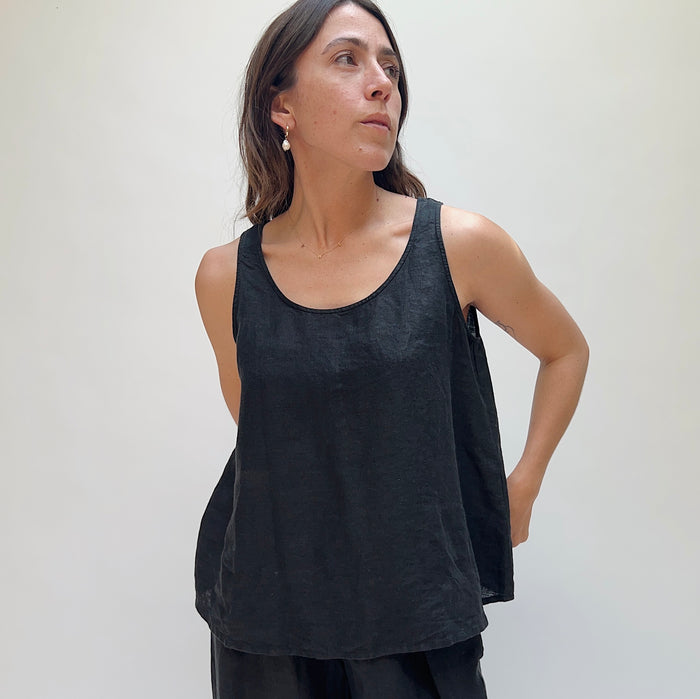 A person looking up and away from the camera with long brown hair wearing a black linen tank top and matching black linen pants.
