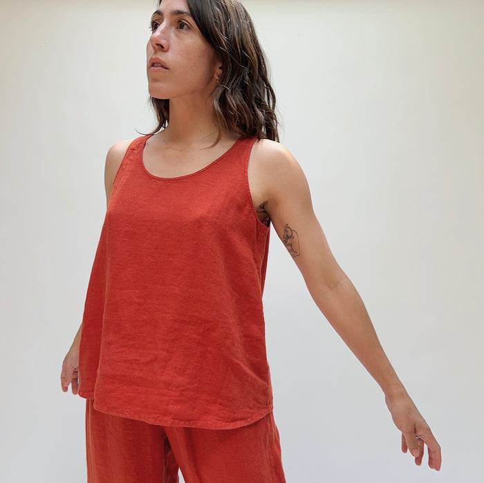 A person wearing a red linen tank top and matching pants, standing against a plain background with her arms held out behind her.