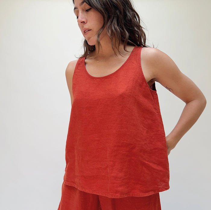 A person wearing a red linen tank top and matching pants, standing against a plain background.