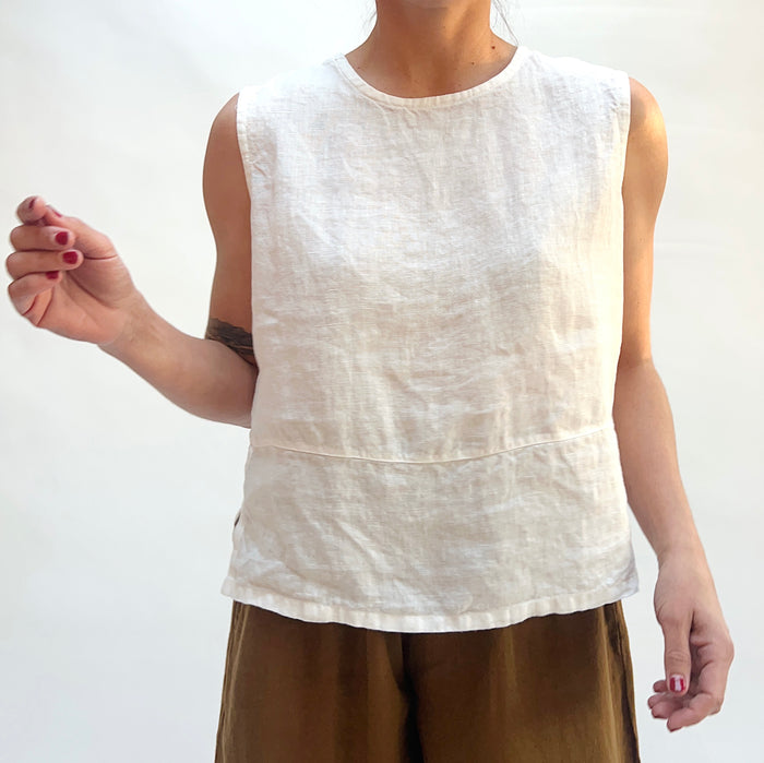 Person wearing a white sleeveless top and brown pants on a plain background