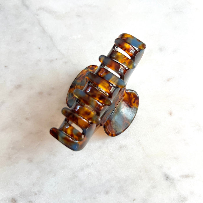A tortoiseshell hair claw clip with brown and amber patterns, resting on a light marble surface.