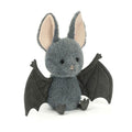 Jellycat Broox Bat plush toy on a white background, showing a round blue-grey fluffy body with large cream-lined ears, black hard eyes, a pink nose, dark outstretched wings, and small dark feet