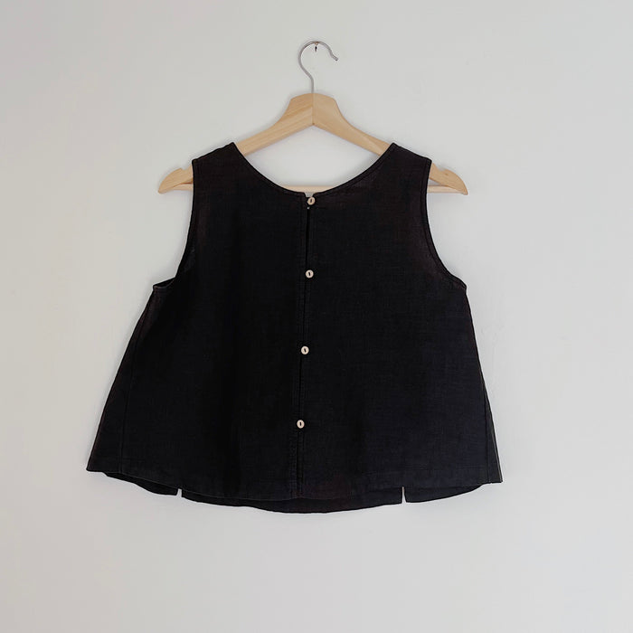 Cropped black linen tank top with buttons down the back, displayed on a wooden hanger against a white background.