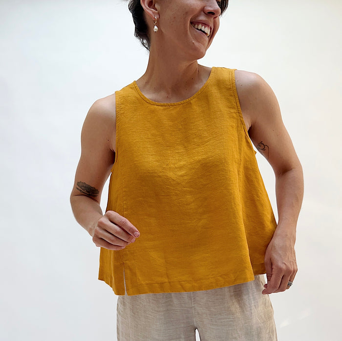 Person wearing a mustard yellow sleeveless top against a white background
