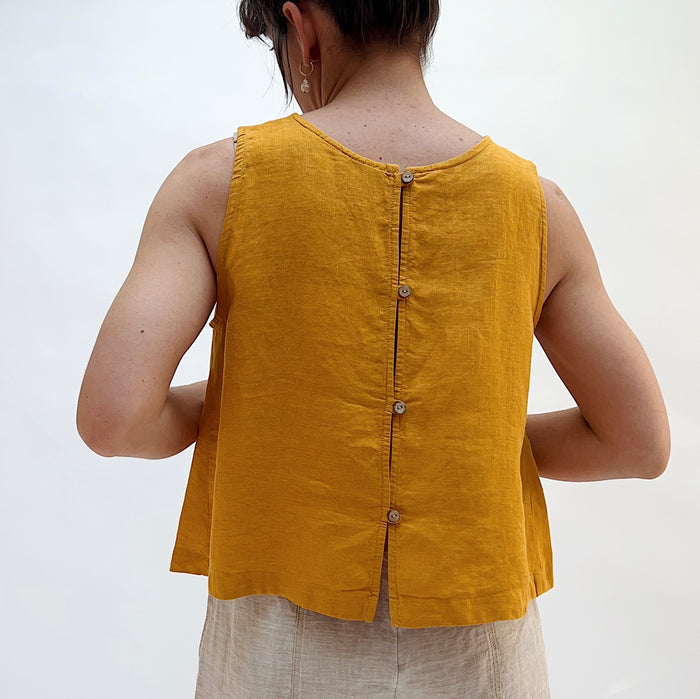 Mustard yellow sleeveless top worn by a person on a white background facing away from the camera. There are wooden buttons down the back of the tank top.
