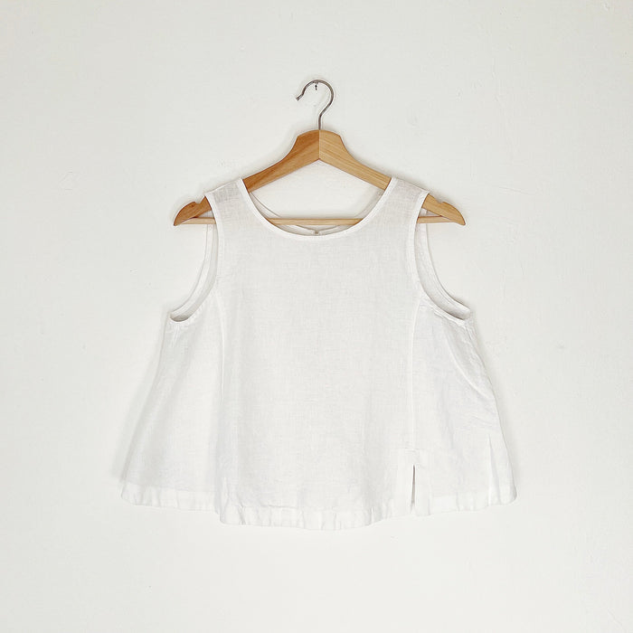 Cropped white linen tank top with buttons down the back and side slits, displayed on a wooden hanger against a white background.