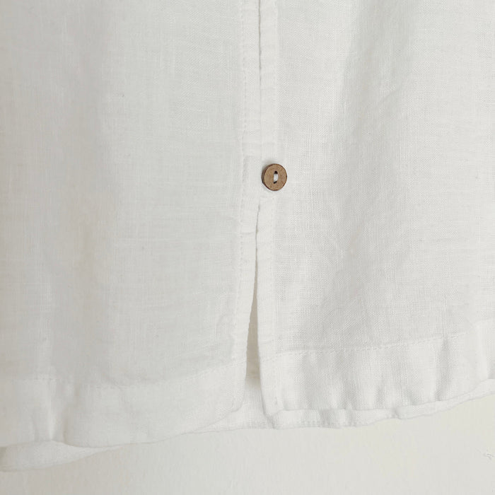 Close up shot of a cropped white linen tank top with buttons down the back and side slits, displayed on a wooden hanger against a white background.