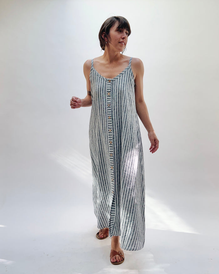 Woman wearing a long, striped linen dress in white and grey on a white background.
