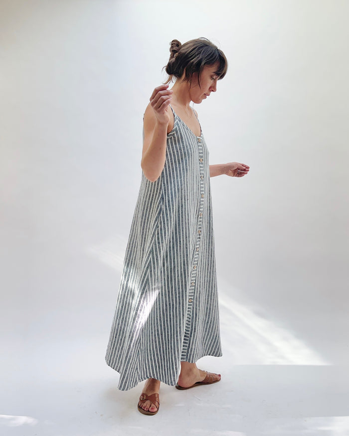 Woman wearing a long, striped linen dress in white and grey on a white background.
