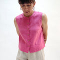 Woman wearing a pink sleeveless linen top with buttons on a white background.
