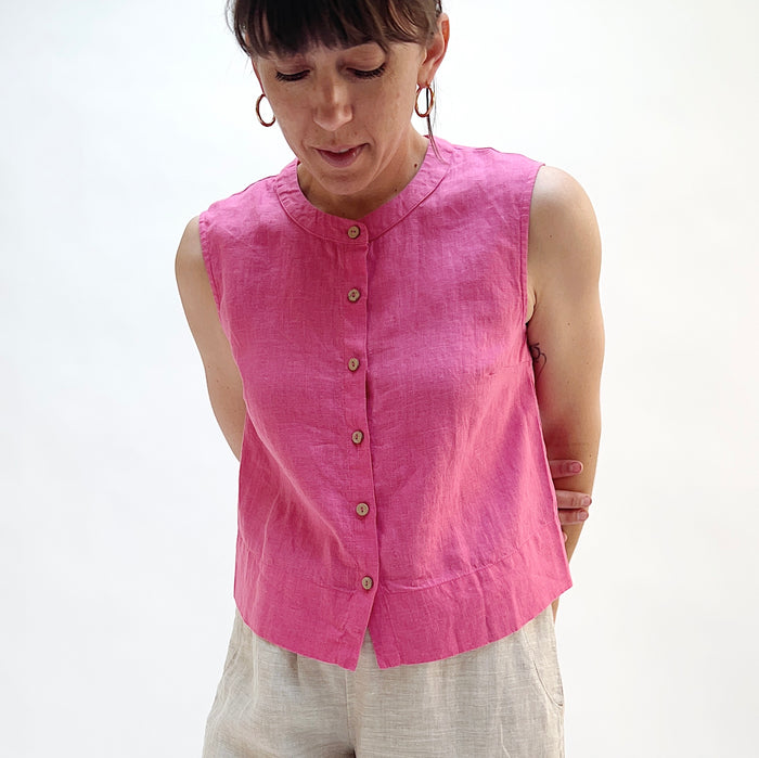 Woman wearing a pink sleeveless linen top with buttons on a white background.