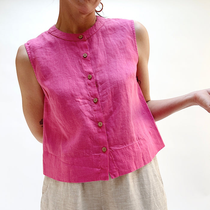 Woman wearing a pink sleeveless linen top with buttons on a white background.