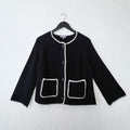 Black knit jacket with white trim on a hanger against a white wall