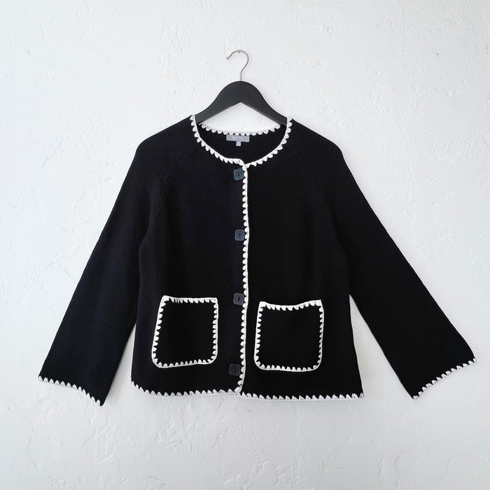 Black knit jacket with white trim on a hanger against a white wall