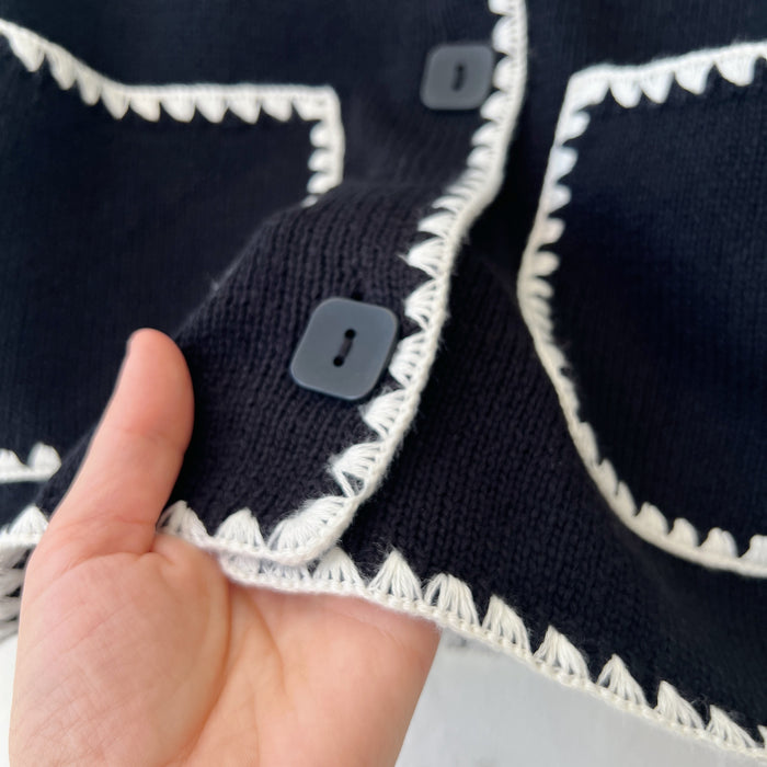 Close-up of a black garment with white trim, held by a hand.