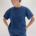 Close front view of model wearing Pacific Cotton nova crop crew tee with hands on hips, showing crew neckline, short sleeves, boxy cropped fit, banded hem, and deep teal color