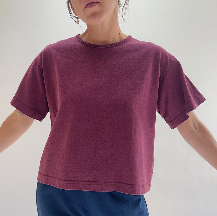 Close front view of model wearing Pacific Cotton rhone crop crew tee, showing ribbed crew neckline, short cuffed sleeves, boxy cropped fit, banded hem, and berry plum color