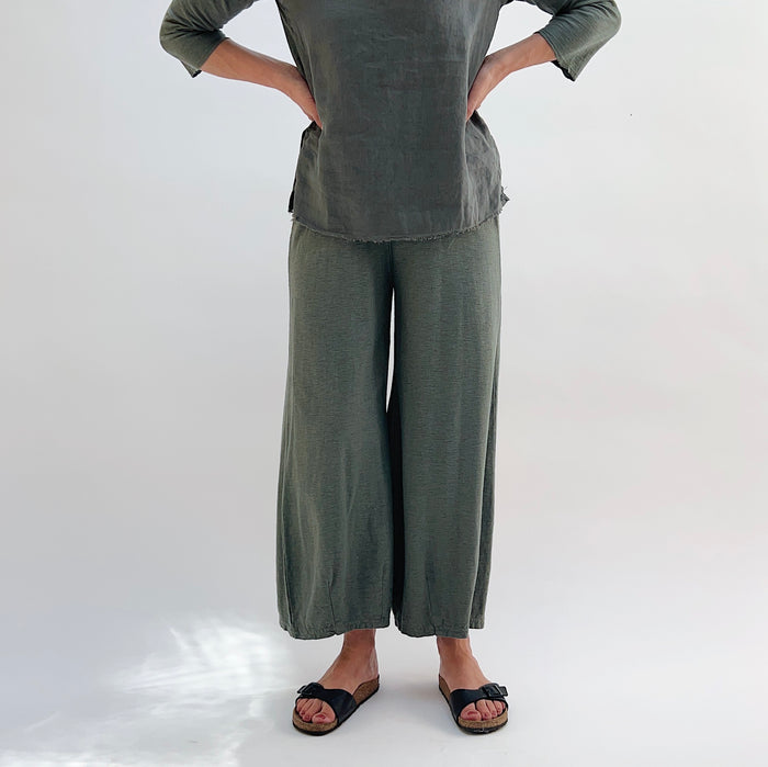 A person wearing a pair of cropped pants with darts at the hemline, made of cotton and linen blend, in a green color.
