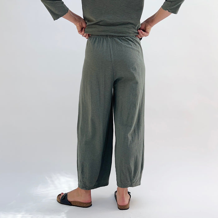 Person wearing green cropped pants on a plain background, viewed from behind