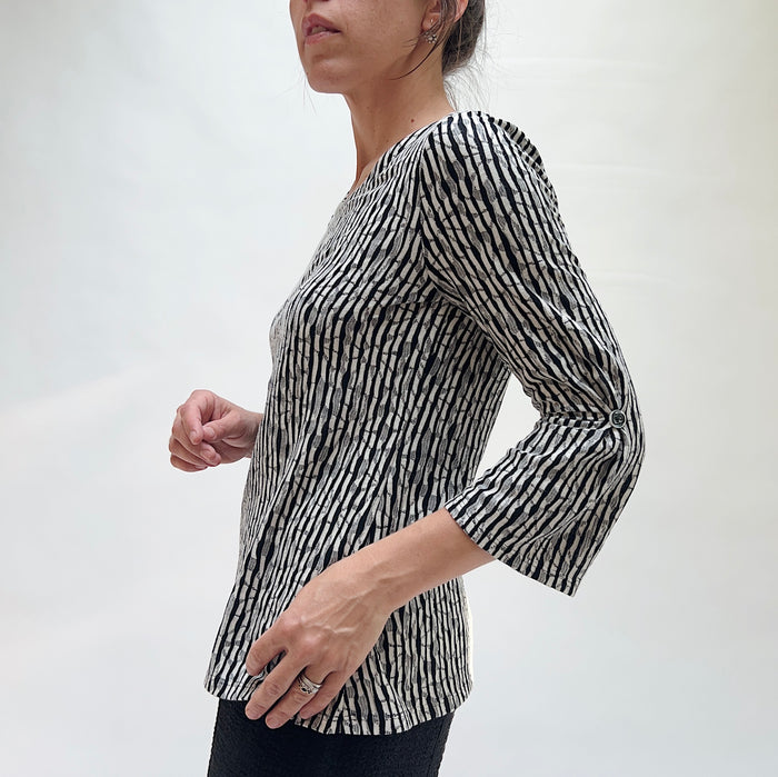Person wearing a black and white patterned long-sleeve top on a plain background seen from the side