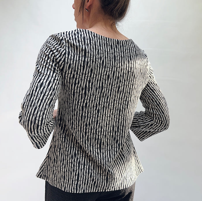 Person wearing a black and white patterned blouse against a plain background seen from behind