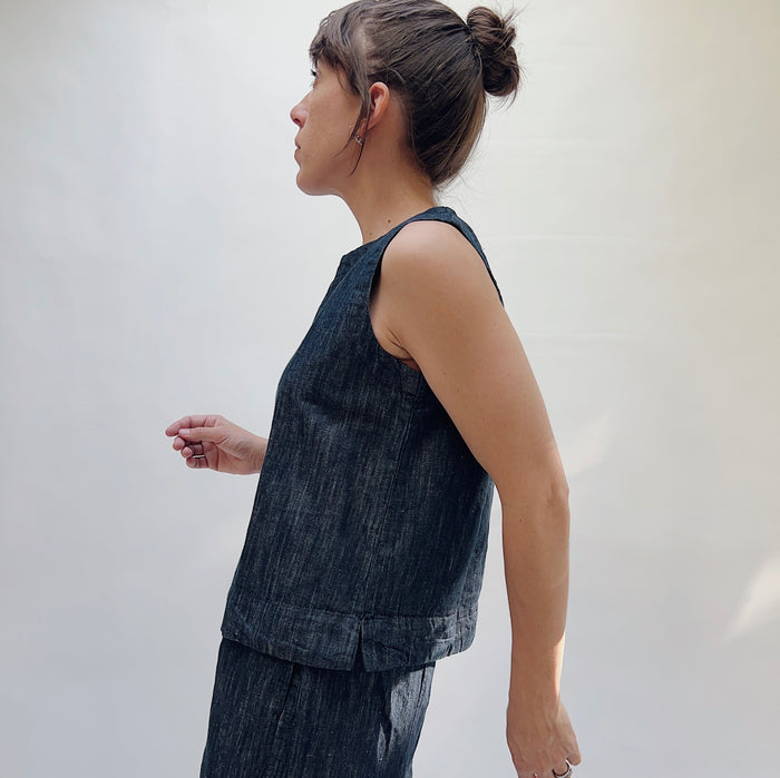 Woman wearing a dark denim sleeveless top and pants against a plain background