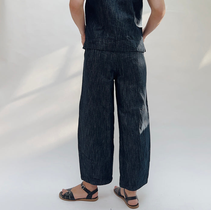 Person wearing a dark denim outfit with wide-leg pants on a white background, viewed from the back