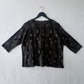 Dark green polka dot blouse on a hanger against a white wall