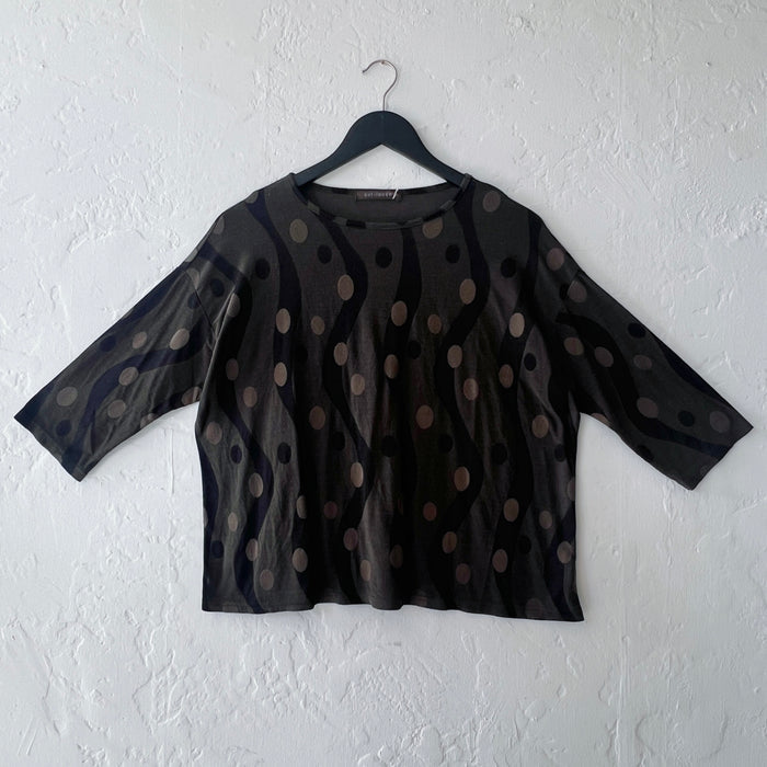 Dark green polka dot blouse on a hanger against a white wall