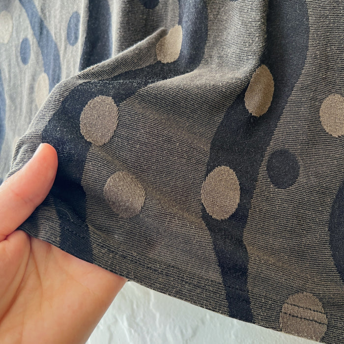 Dark green fabric with beige polka dots held by a hand against a neutral background