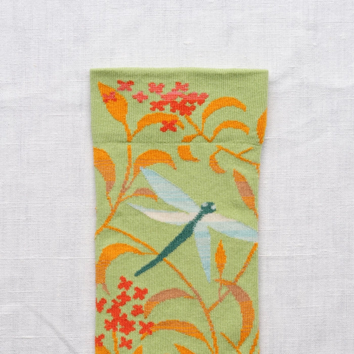 Close-up of the ankle portion of the socks with floral and dragonfly design on a light background