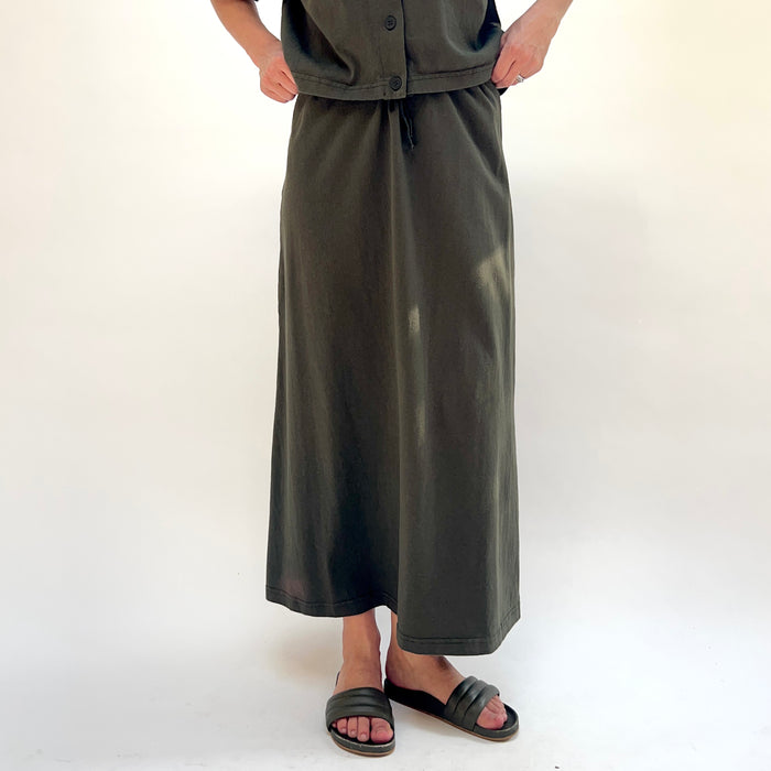 Person wearing a long dark green skirt and top on a white background