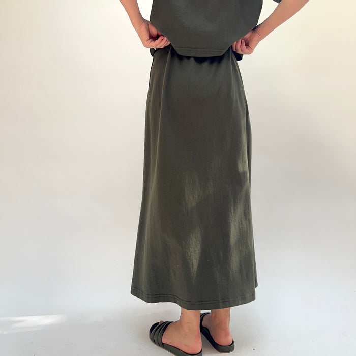 Person wearing a long green skirt on a white background, viewed from the back