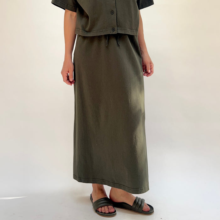 Person wearing a long olive green skirt with a plain background
